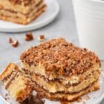 A square slice of coffee cake served on a white dish with a fork that has just taken a bite off the corner