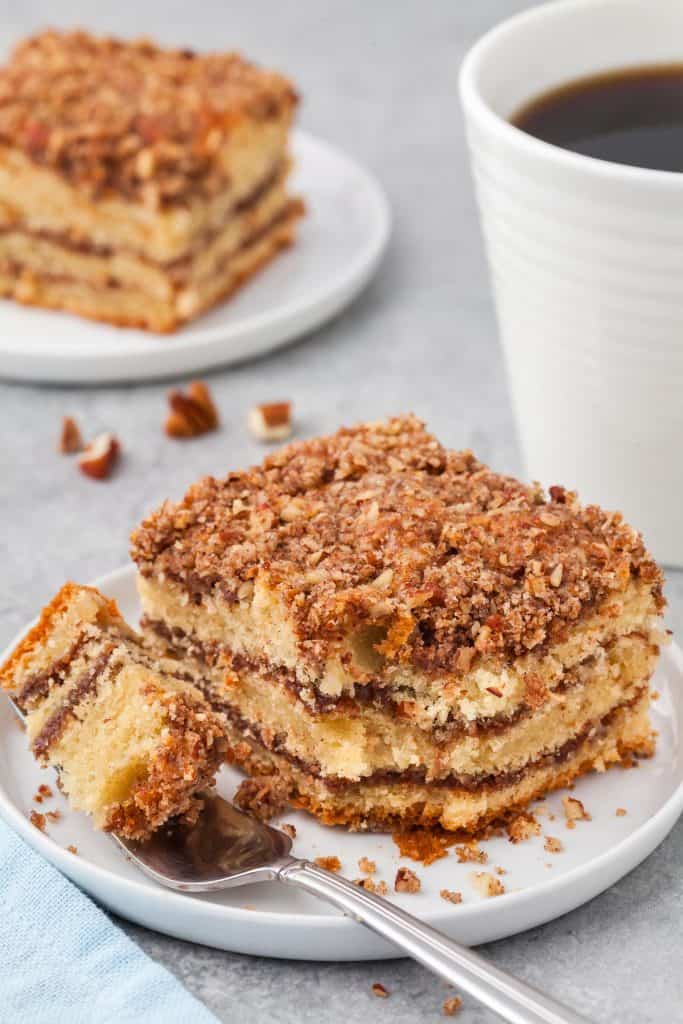 square slice of cinnamon coffee cake served on a plate with a fork full of cake resting on the plate.