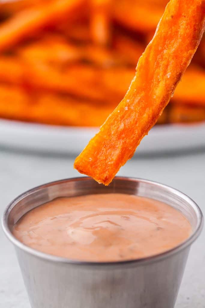 Close up shot of a sweet potato fry just about to be dipped in chipotle mayo