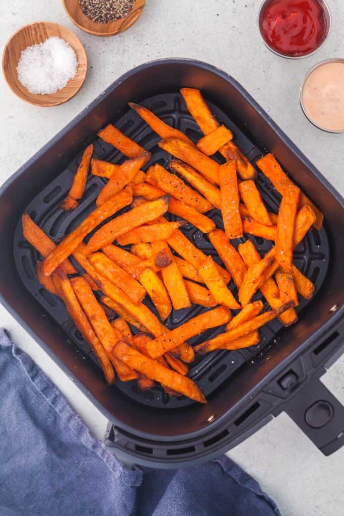 Sweet potato fries cooked and crispy in the air fryer basket with a small sprinkling of salt and pepper