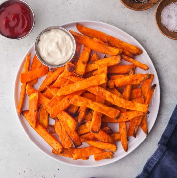 Air fryer frozen sweet potato fries served on a white plate with ketchup and mayonnaise dipping sauces