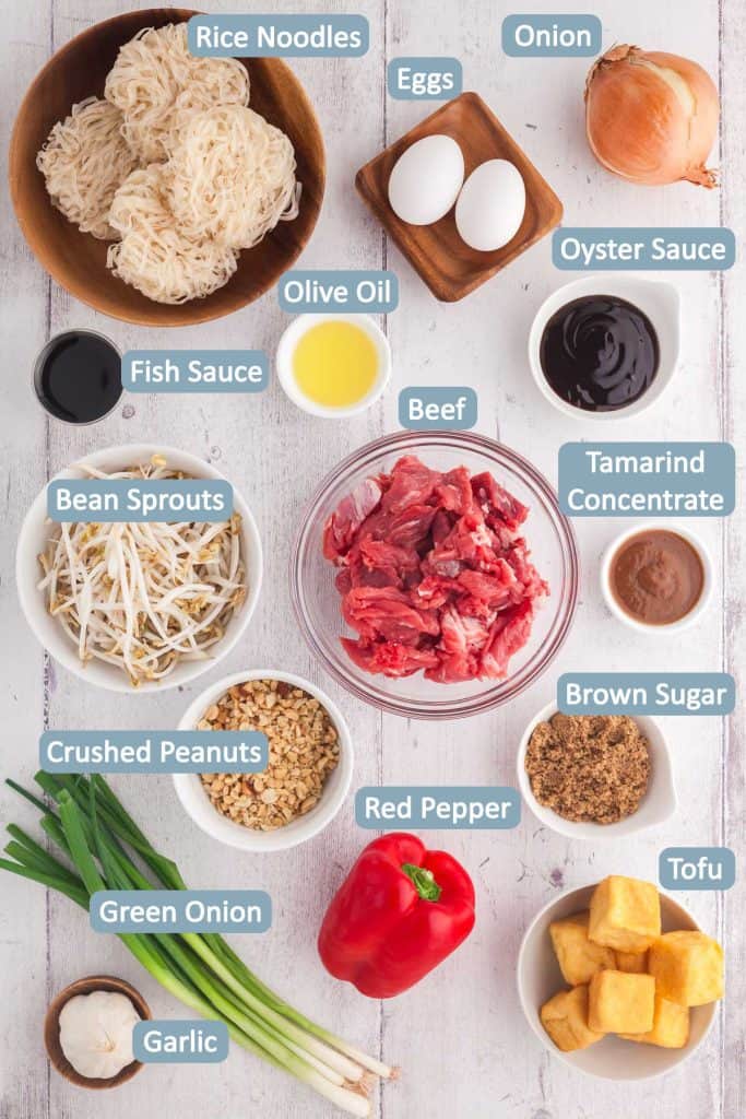 Overhead shot of ingredients used in beef pad thai including: rice noodles, eggs, onion, green onions beef, bean sprouts, red pepper, tofu, brown sugar, oyster sauce, fish sauce, garlic, tamarind concentrate, and olive oil