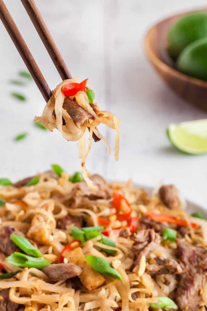 Side shot of pad thai being lifted off the plate with chopsticks.