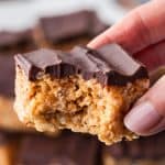 A close up shot of a chocolate and peanut butter rice krispie treat that is being held by hand and a bite missing.
