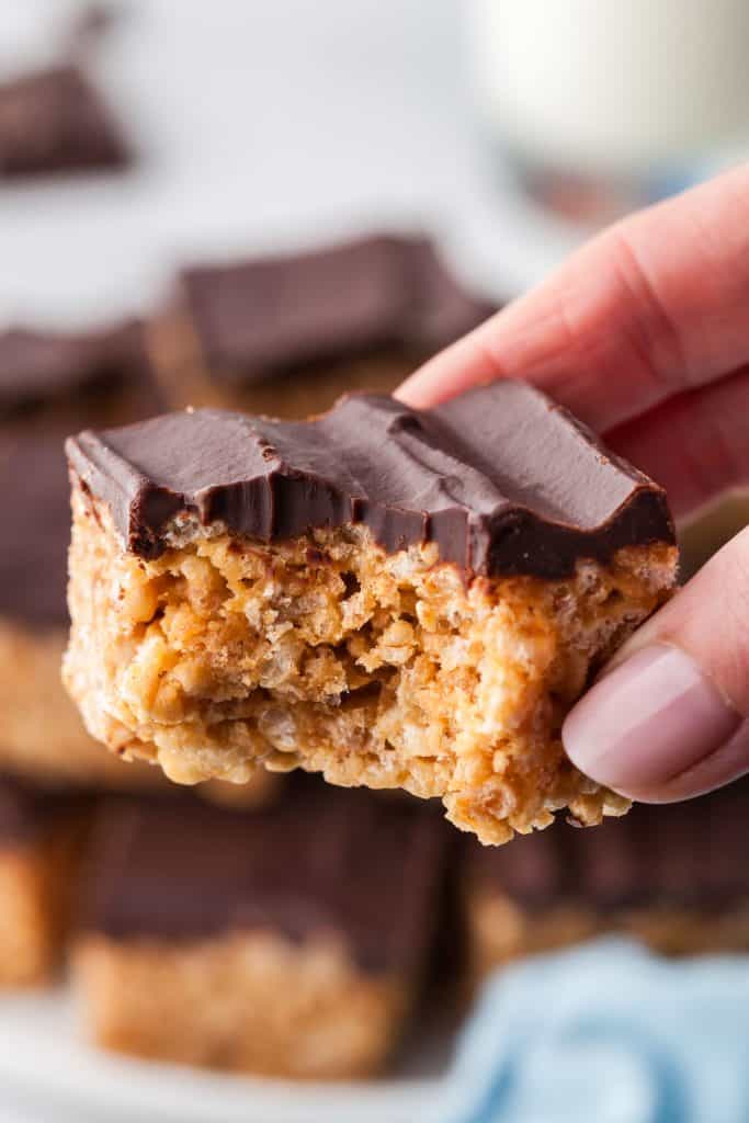 A close up shot of a chocolate and peanut butter rice krispie treat that is being held by hand and a bite missing.