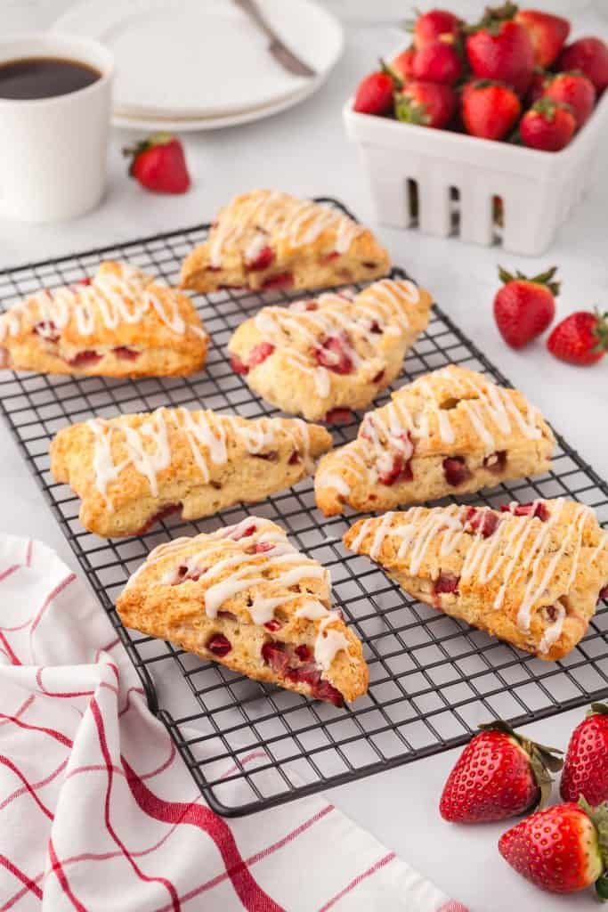 45 degree angle of 7 strawberry scones cooling on a cooling rack with fresh strawberries scattered around