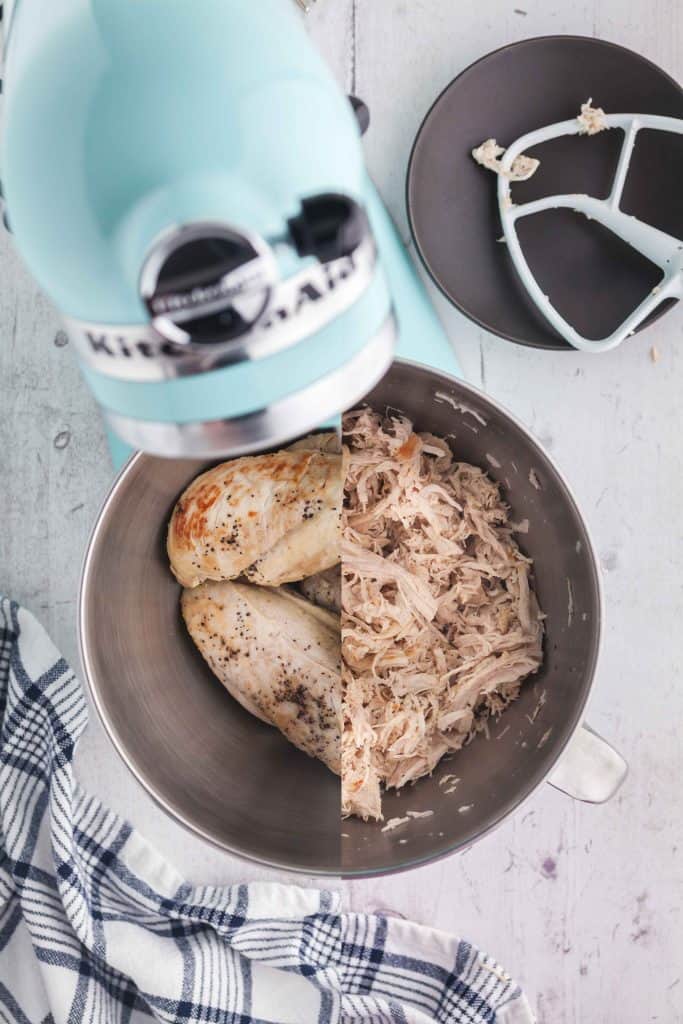 Split overhead shot looking into the mixing bowl where the left hand side is the cooked chicken breasts and the right hand side is the shredded chicken after the mixer shreds it.