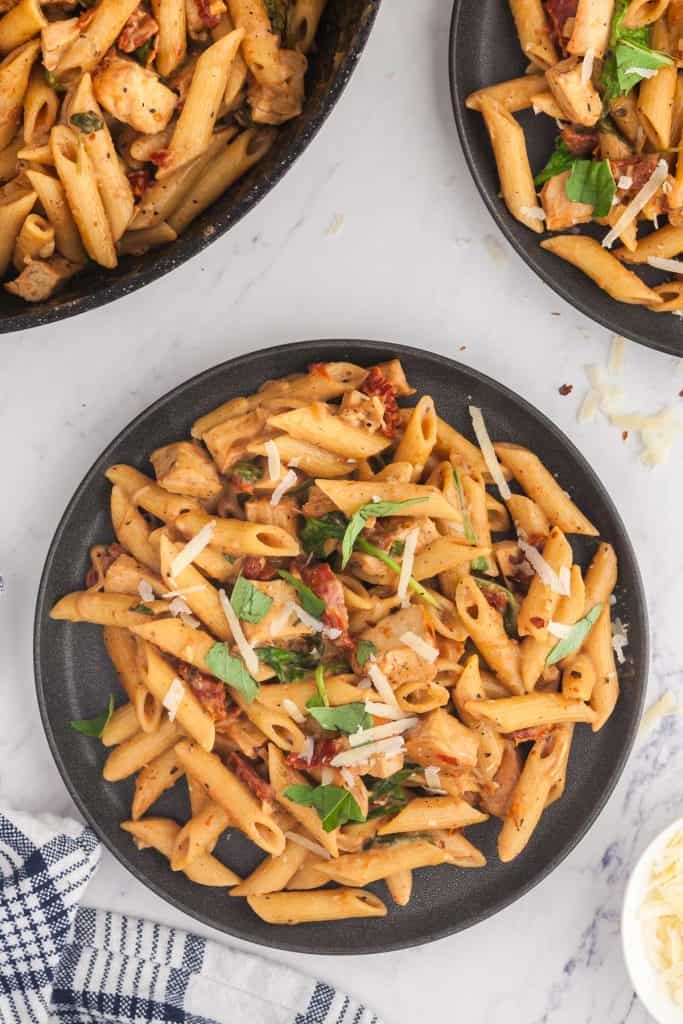 Overhead shot of the pasta on a plate garnished with fresh basil and shredded parmesan. The top right hand corner has another plate of pasta peeking into the frame and the upper left corner has the frypan full of pasta peeking into the frame.