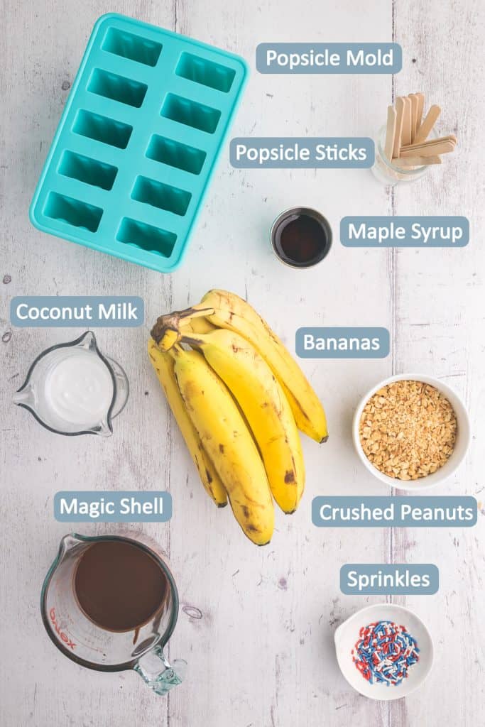 Overhead shot of ingredients used to make Banana Popsicles - bananas, coconut milk, maple syrup, magic shell, crushed peanuts, sprinkles, popsicle mold, popsicle sticks