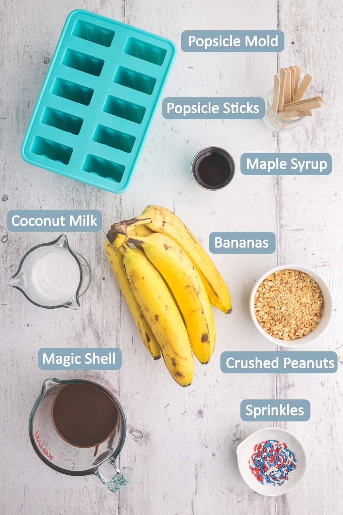 Overhead shot of ingredients used to make Banana Popsicles - bananas, coconut milk, maple syrup, magic shell, crushed peanuts, sprinkles, popsicle mold, popsicle sticks