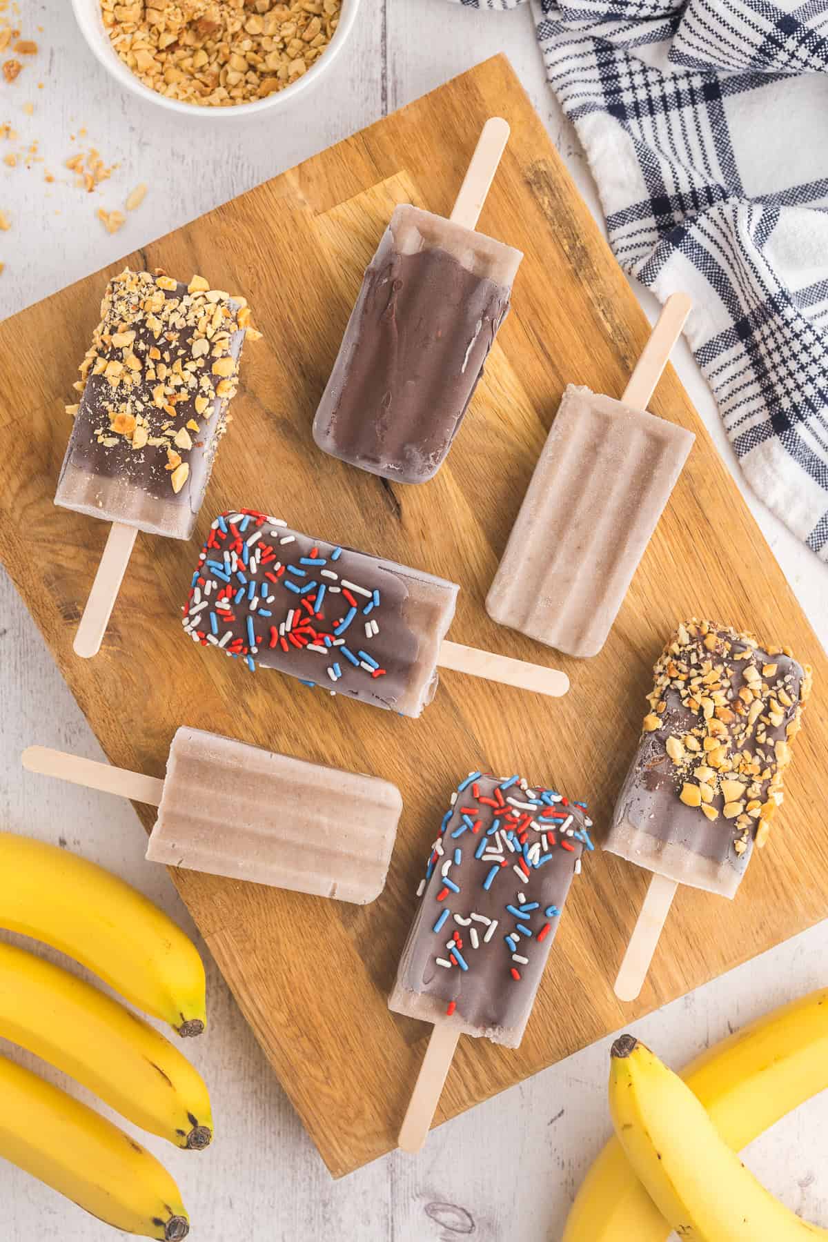 banana popsicles with sprinkles and nuts on a cutting board