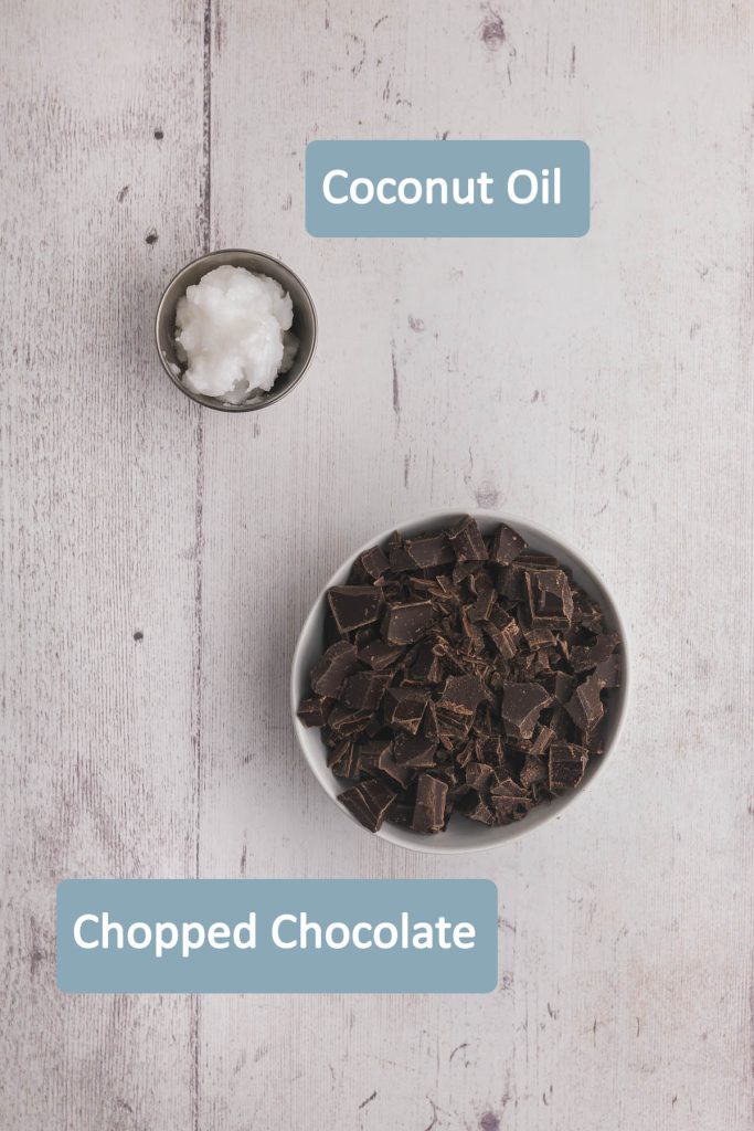 Overhead ingredient shot showing what is needed to make Magic Shell. A small bowl of chopped chocolate, and 3 tablespoons of coconut oil in a metal pinch bowl.