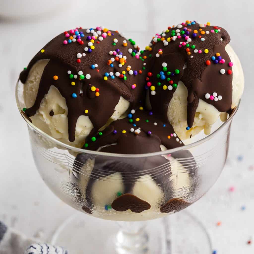 a glass dessert bowl filled with three scoops of vanilla gelato and topped with magic shell and sprinkles
