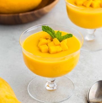 45 degree angle view of mango pudding served in a delicate glass dessert bowl, garnished with diced mangoes and a sprig of fresh mint