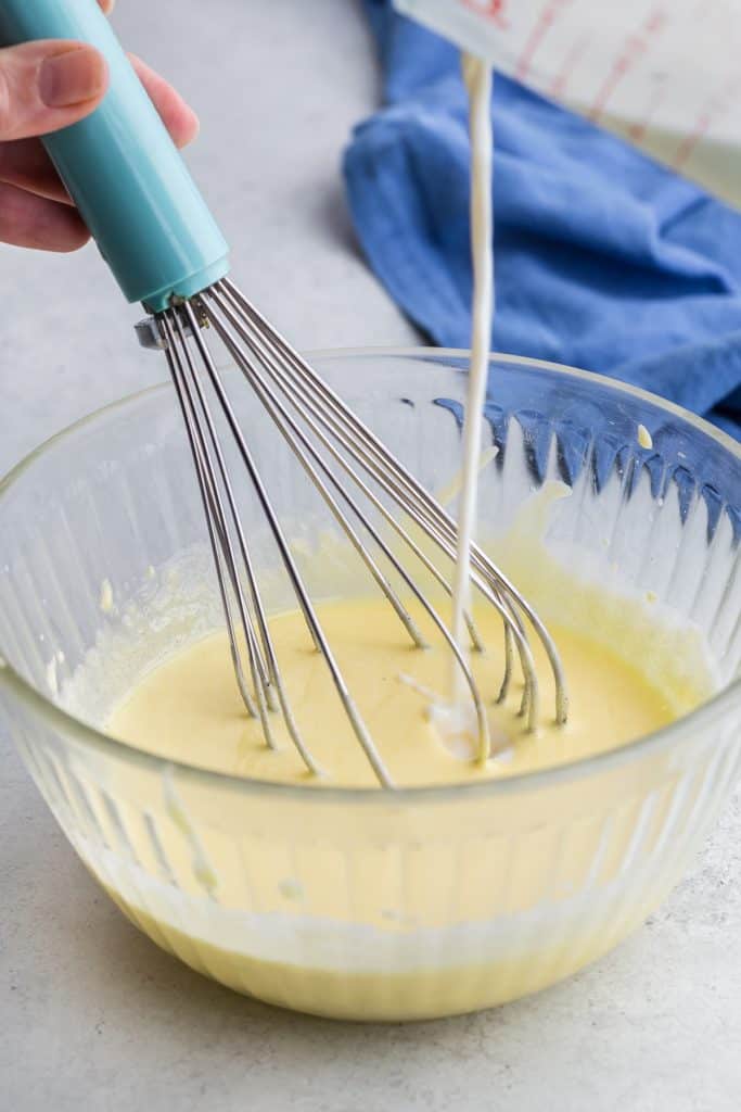 Side view shot of the egg yolk/sugar mixture being tempered with hot milk for the vanilla gelato. Whisking constantly while the hot milk is being poured in.