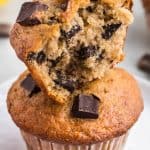 Close up view of a torn open half banana chocolate chunk muffin stacked on top of another muffin. Lots of chocolate chunks can be seen in the interior.