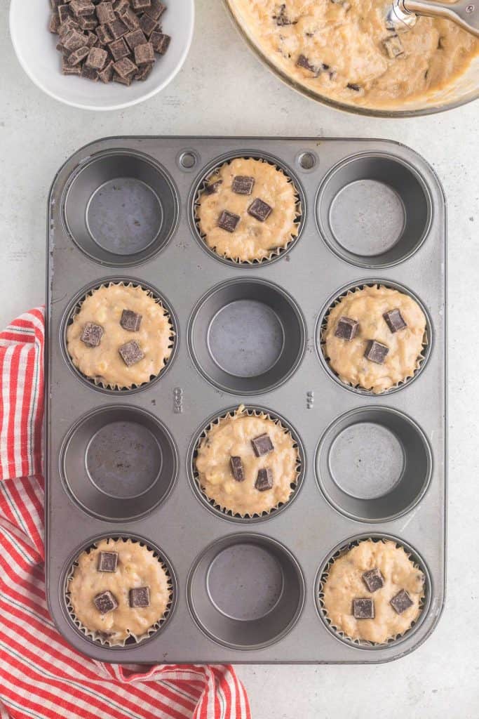 Overhead view of muffin tin with every other hole filled with banana chocolate chunk muffin batter.