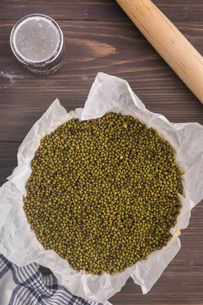 Overhead shot of Chocolate Caramel tart tart shell filled with parchment paper, and mung beans so it is ready to be baked in the oven