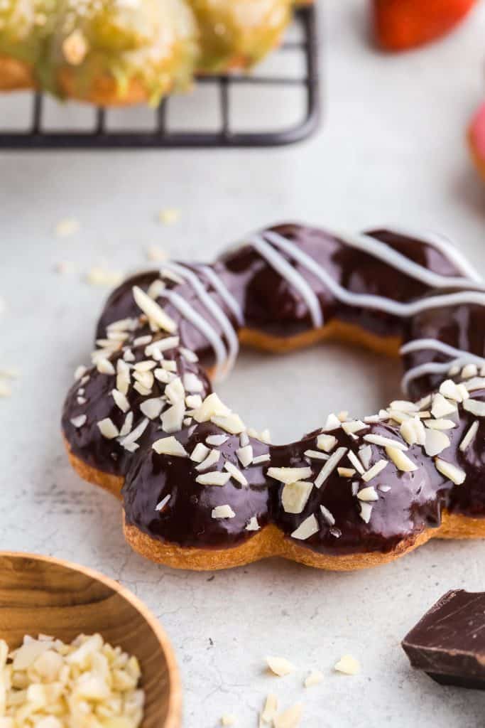 Side shot of a mochi donut dipped in chocolate ganache, sprinkled with slivered almonds on one side, and piped white chocolate on the other