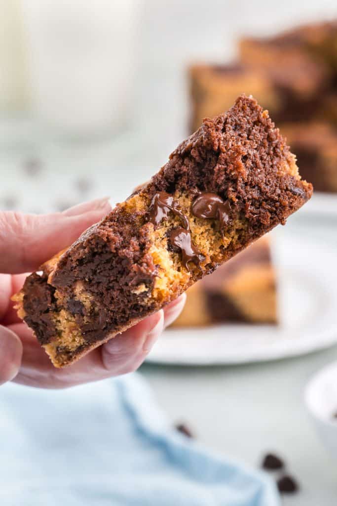 Close up shot of a brookie with a bite out of it being held up close to the camera. You can see some melty chocolate chips in the cookie dough portion.