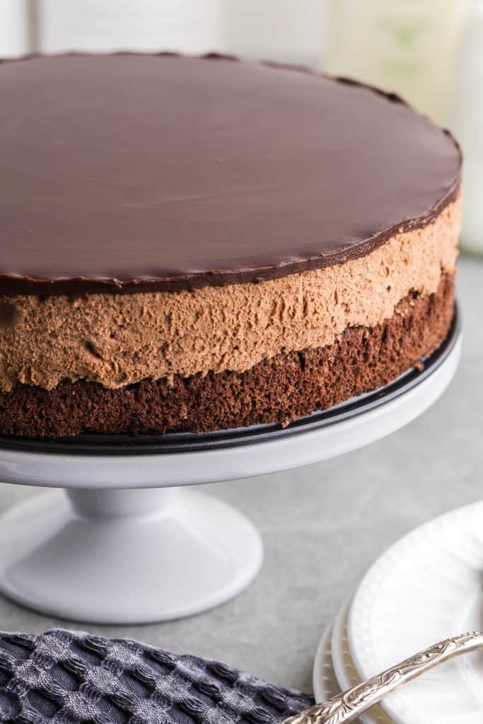 side profile of the chocolate mousse cake up on a cake pedestal before being sliced into. You can see the distinct three chocolate layers around the outside.