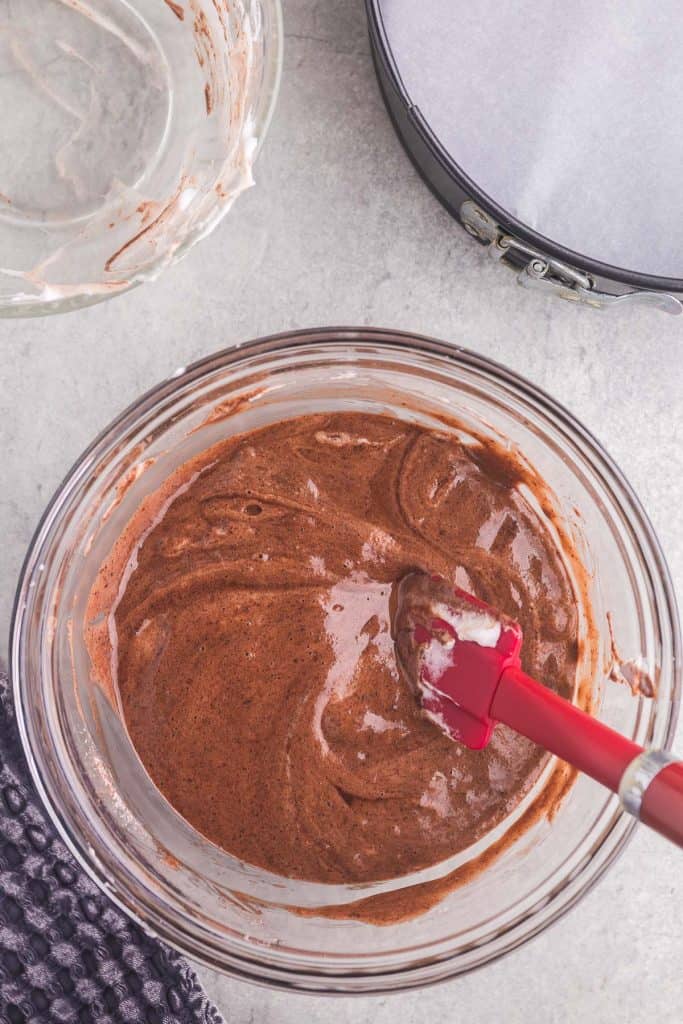 The chocolate chiffon cake batter after the egg whites have been added. The batter is a light brown with a fluffy texture. In the upper right hand corner is the prepared springform pan.