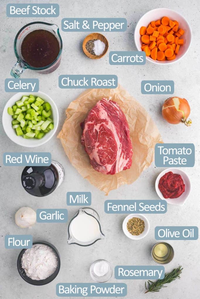 Overhead shot of all the ingredients needed to make beef stew with dumplings. Ingredients are: beef stock, salt and pepper, carrots, onion, celery, chuck roast, red wine, tomato paste, fennel seeds, garlic, milk, flour, baking powder, olive oil, and rosemary.
