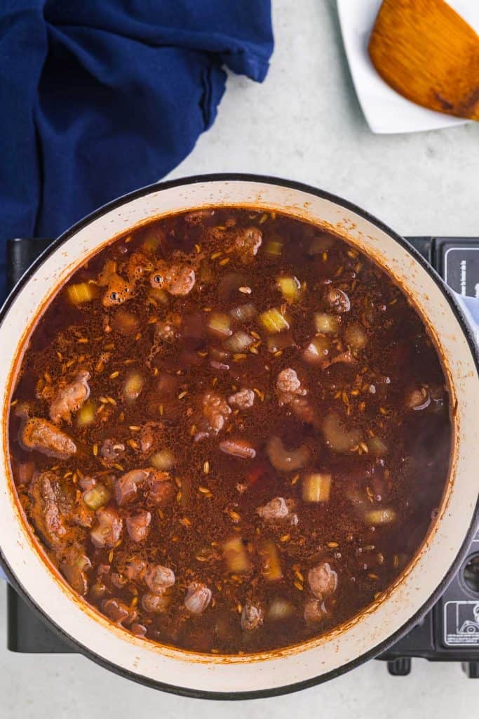 Overhead shot of the Dutch oven filled with all the ingredients for the beef stew, it is a nice rich brown color with chunks of veggies and beef. The pot is ready to go in the oven to cook.
