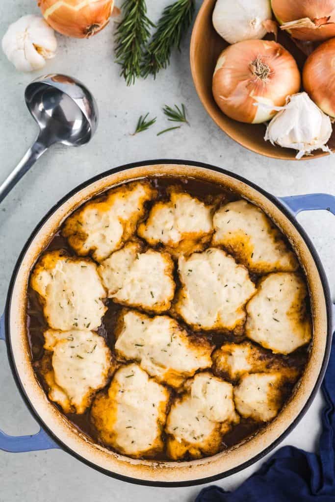 Overhead shot of the finished beef stew and dumplings. The rich brown stew is covered by 12 fluffy white rosemary dumplings.