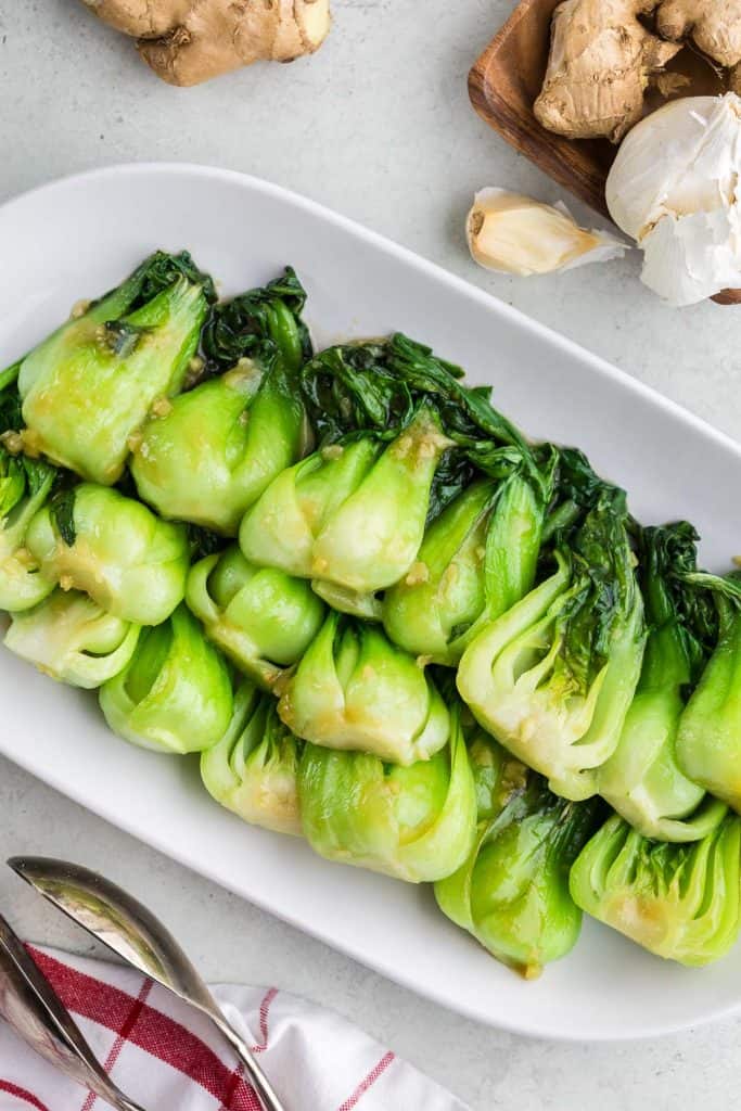 Overhead shot of cooked Shanghai bok choy served on a white platter.  Garlic and ginger are poking into the picture from the top.