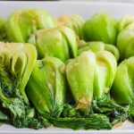 Close up view of cooked vibrant green shangai bok choy oriented all in the same vertical direction and covered in a light sauce with small bits of ginger.