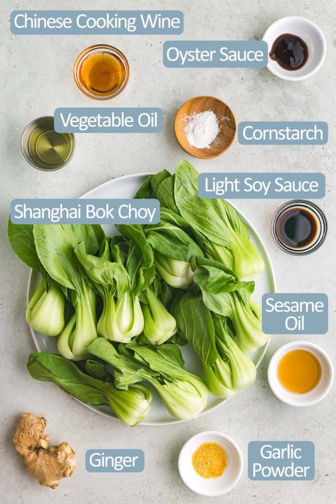 Overhead shot of all the ingredients needed to make Shanghai Bok Choy.  Ingredients include: green leafy baby Shanghai bok choy, vegetable oil, Chinese cooking wine, oyster sauce, light soy sauce,  cornstarch, sesame oil, garlic powder, and fresh ginger.