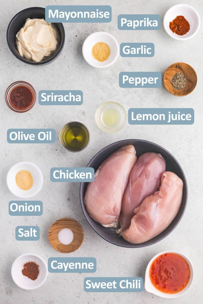 Overhead shot of the ingredients needed in making these bang bang chicken skewers. Ingredients include: chicken breast or thigh, table salt, cracked black pepper, garlic powder, onion powder, paprika, cayenne, mayonnaise, sweet chili sauce, sriracha, and lime juice.