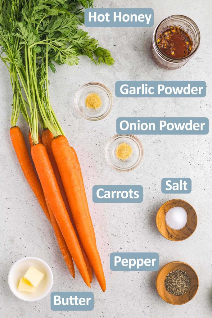 Overhead shot of all the ingredients used in making hot honey carrots. Ingredients include fresh carrots, hot honey sauce, garlic powder, onion powder, salt, pepper, and butter.