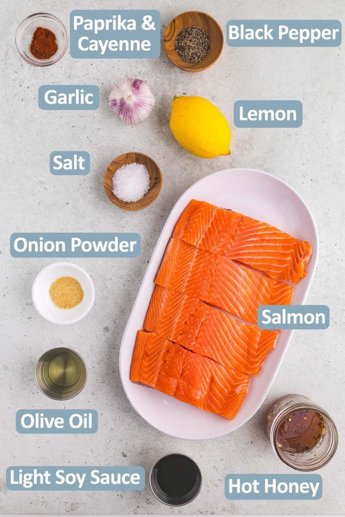 Overhead shot of the ingredients needed to make hot honey salmon. Ingredients include: Salmon, garlic, lemon juice, salt, cayenne, paprika, black pepper, onion powder, olive oil, light soy sauce, and hot honey.