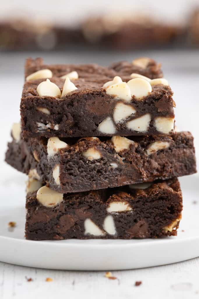 Close up side shot of three chocolate chocolate cookie bars stacked on top of each other. They are each a lovely chocolate brown color studded with plenty of white chocolate chips.