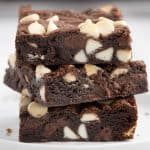 Close up side shot of three chocolate chocolate chip cookie bars stacked on top of each other. The bars are a deep chocolate color studded with plenty of white chocolate chips.