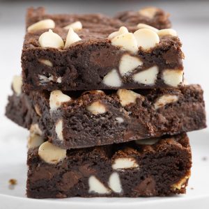 Close up side shot of three chocolate chocolate chip cookie bars stacked on top of each other. The bars are a deep chocolate color studded with plenty of white chocolate chips.