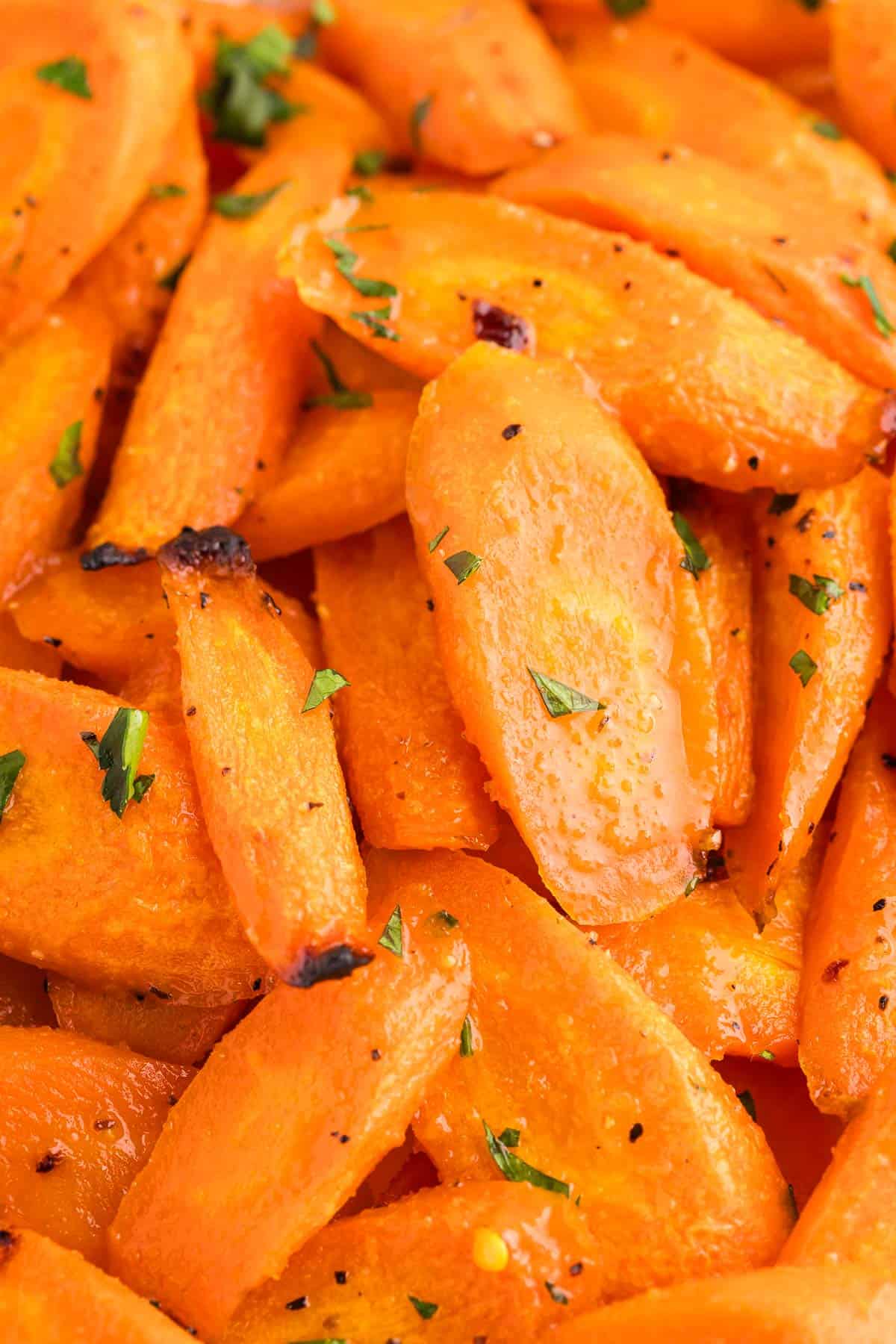 Close up overhead view of bright orange hot honey carrots. Just a little black charring on some edges from the roasting and garnished with fresh chopped parsley.