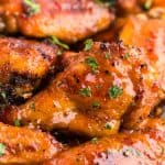Close up shot of hot honey chicken wings. The wings are golden brown and have a shiny gleam from the hot honey sauce that coats them. Chopped fresh parsley is used to garnish them and give a green pop of color.