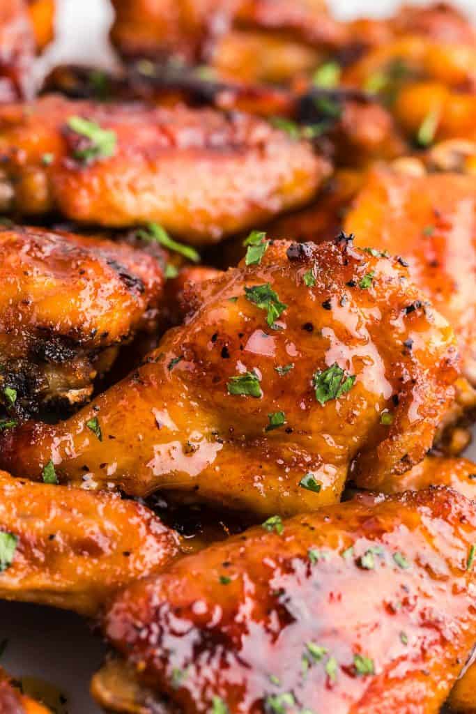 Close up shot of hot honey chicken wings. The wings are golden brown and have a shiny gleam from the hot honey sauce that coats them. Chopped fresh parsley is used to garnish them and give a green pop of color.