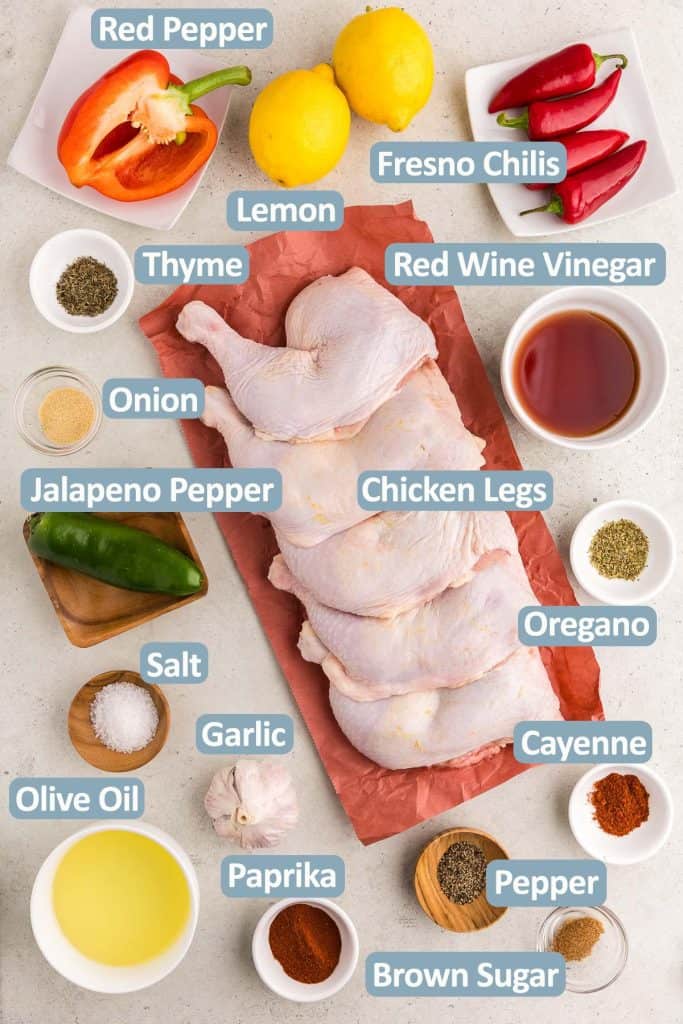 Overhead shot of all the ingredients needed to make Portuguese Chicken.  Ingredients include, red bell pepper, lemons, Fresno peppers, oregano, onion powder, jalapeno pepper, red wine vinegar, thyme, paprika, salt, pepper, cayenne, olive oil, fresh garlic, whole chicken legs, and brown sugar.