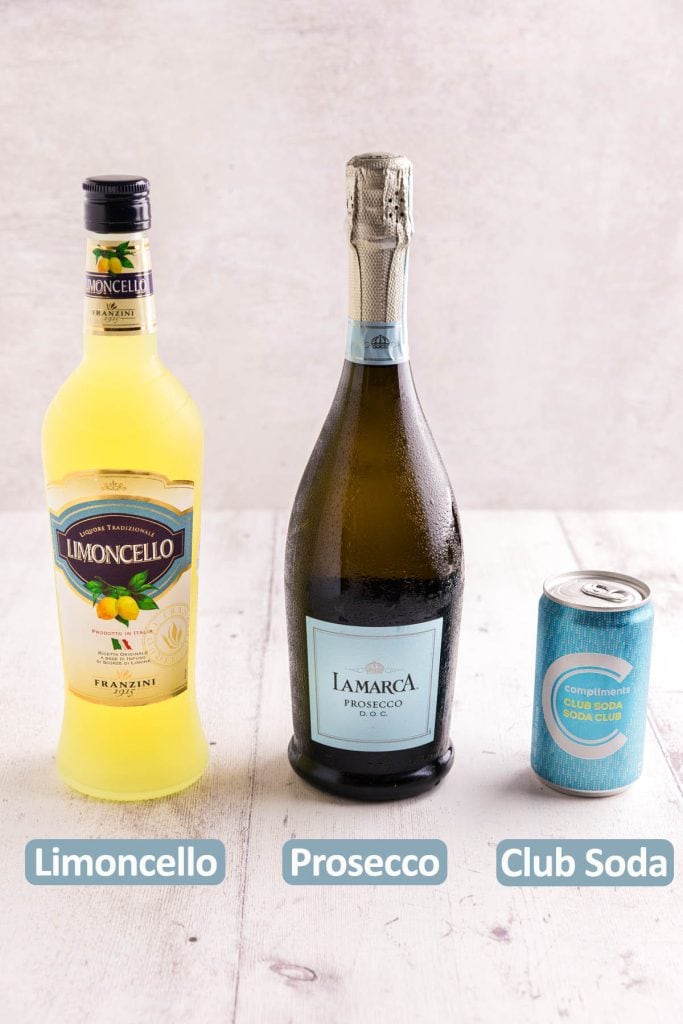 Ingredients needed to make a Limoncello Spritz. On the left is a yellow bottle of limoncello, in the middle is a bottle of prosecco, and on the right is a small can of club soda.