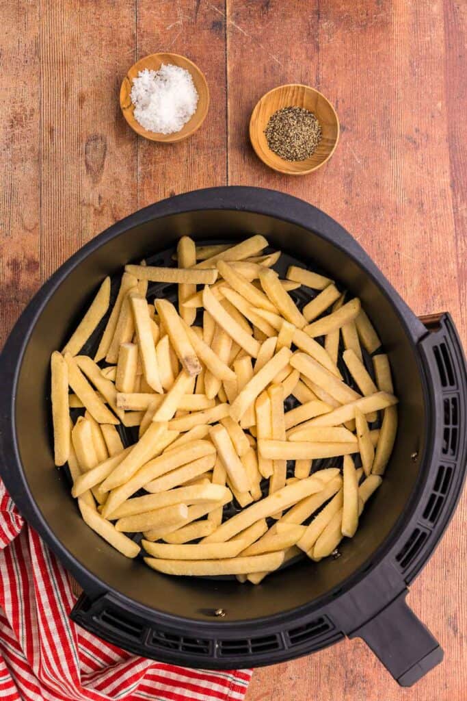 overhead shot of an air fryer basket filled with a shallow layer of frozen french fries getting ready to be cooked.  