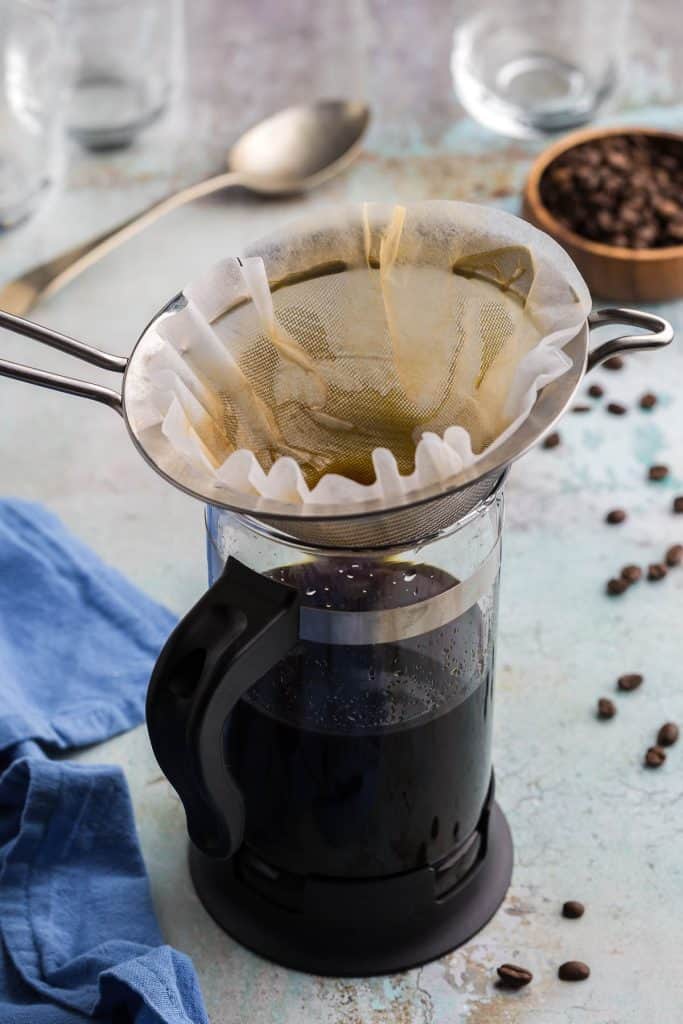 45 degree angle shot of the second filtration for the cold brew concentrate. A coffee filter is sitting in a fine mesh sieve over a jar for the 2nd filtration of cold brew concentrate.