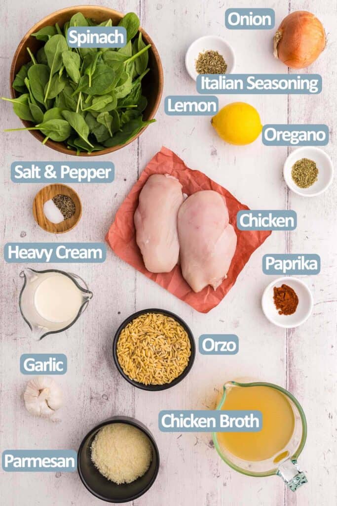Overhead shot of the ingredients used in making Lemon Chicken and Orzo. Ingredients are: Fresh spinach, onion, Italian Seasoning, Dried Oregano, Fresh Lemon, salt and pepper, Chicken breasts, Paprika, Heavy cream, Garlic, shredded parmesan, Chicken broth, and orzo.