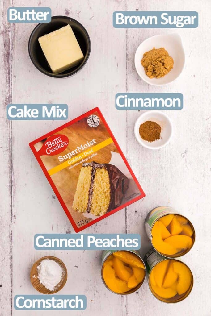 Overhead shot of the ingredients needed to make peach cobbler with cake mix. Ingredients are yellow cake mix, butter, brown sugar, cinnamon, cornstarch and canned peaches.