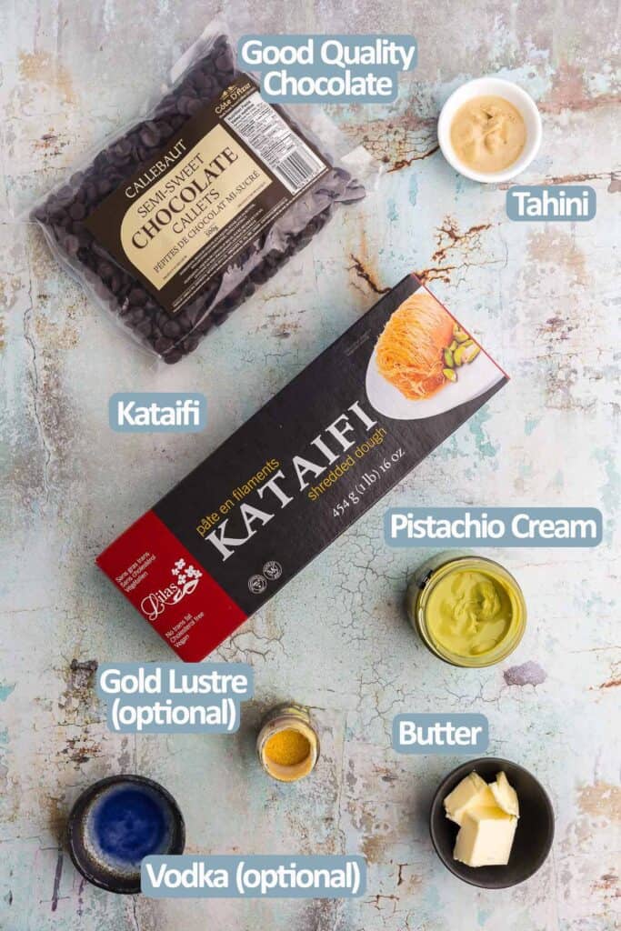 Overhead shot of the ingredients used to make a Dubai Chocolate Bar.  Ingredients are: Good quality chocolate, Tahini, Kataifi, Pistachio cream, Butter, Gold Luster, and vodka. 