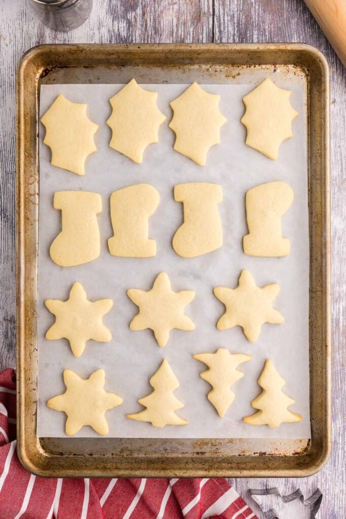 Overhead shot of a stainless steel baking sheet lined with white parchment and filled with cooked Christmas sugar cookies.  All of them are just slightly browned.