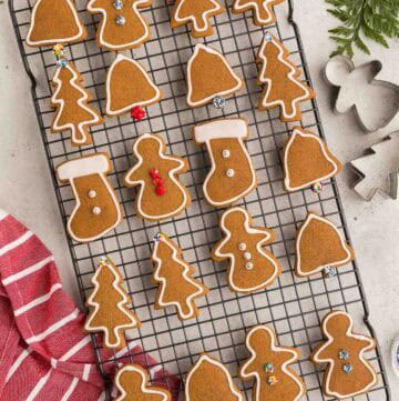 Overhead picture of a cooling rack filled with gingerbread cookies all outlined with white royal icing. Two of the stocking shaped cookies have been flooded with icing, and some of the cookies have sprinkles on them.
